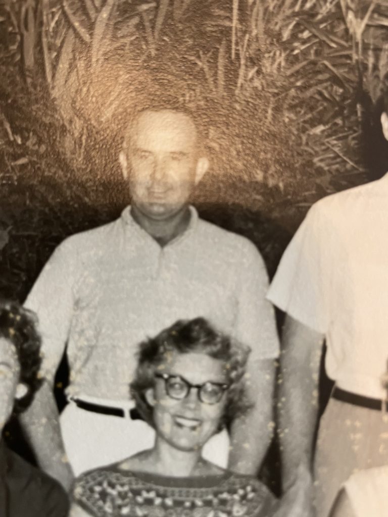 Black and white photo of Gerry Mayo Beveridge, seated smiling, with husband David standing behind. 