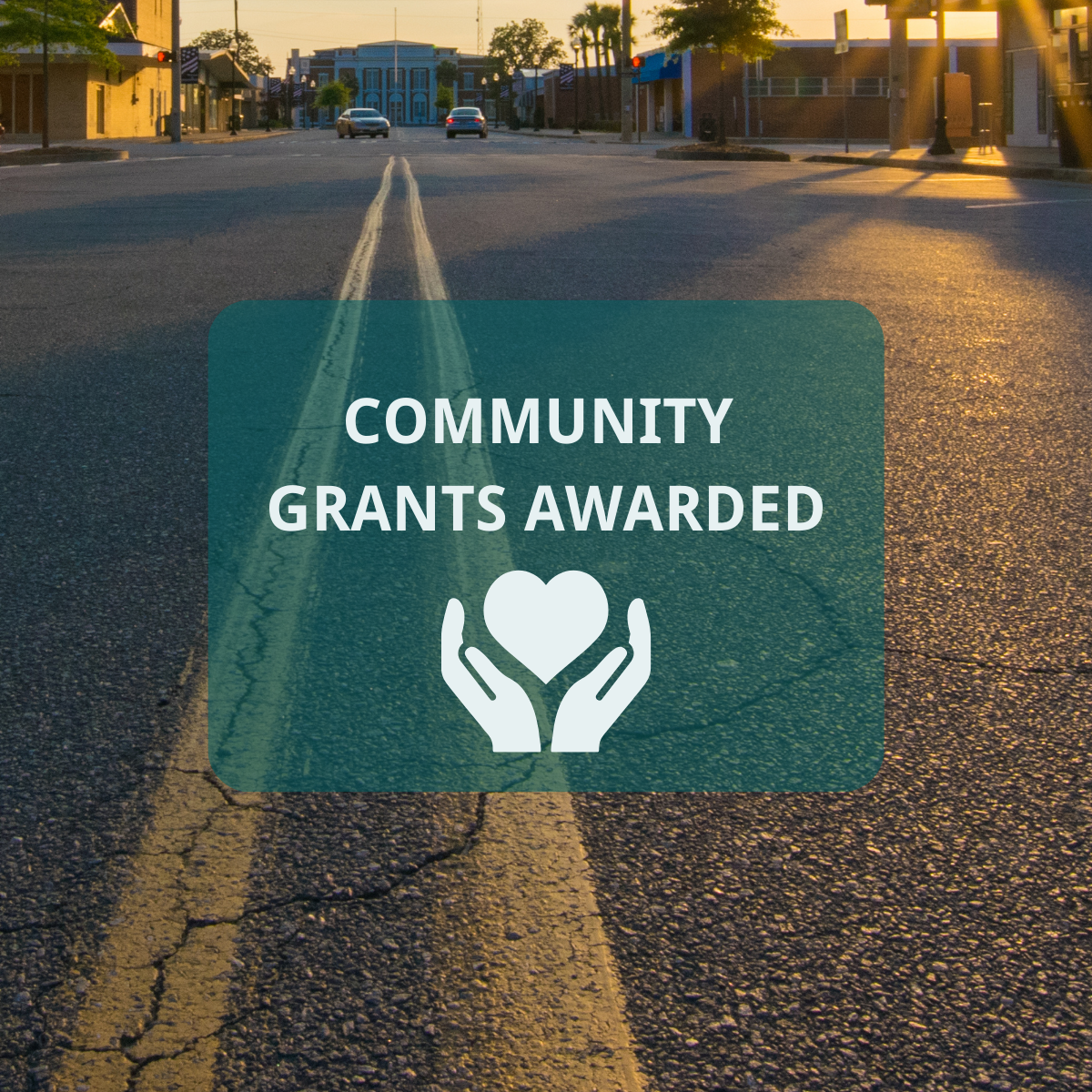 An image of a road through a small town with text that reads Community Grants Awarded above a graphic of two hands holding a heart.