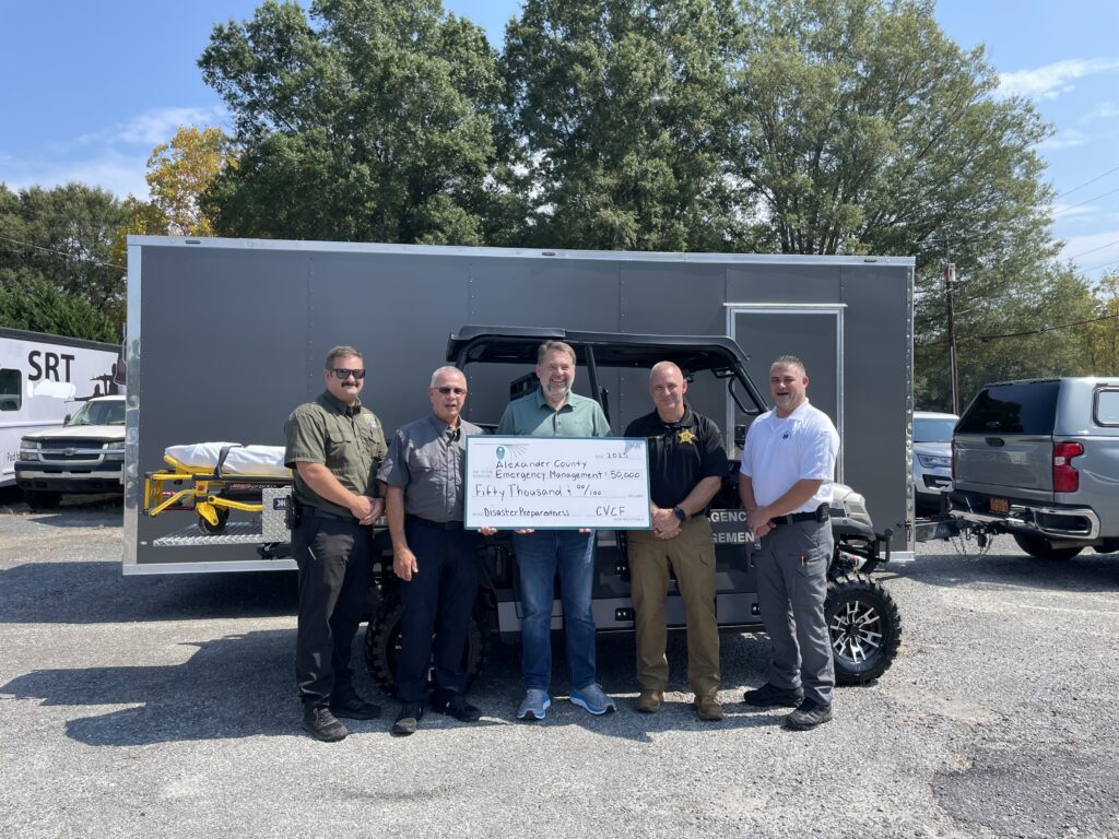 Five men standing in front of a utility terrain vehicle holding a check.