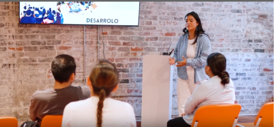 Iza Herrara presents to a group in a bright room with orange chairs.