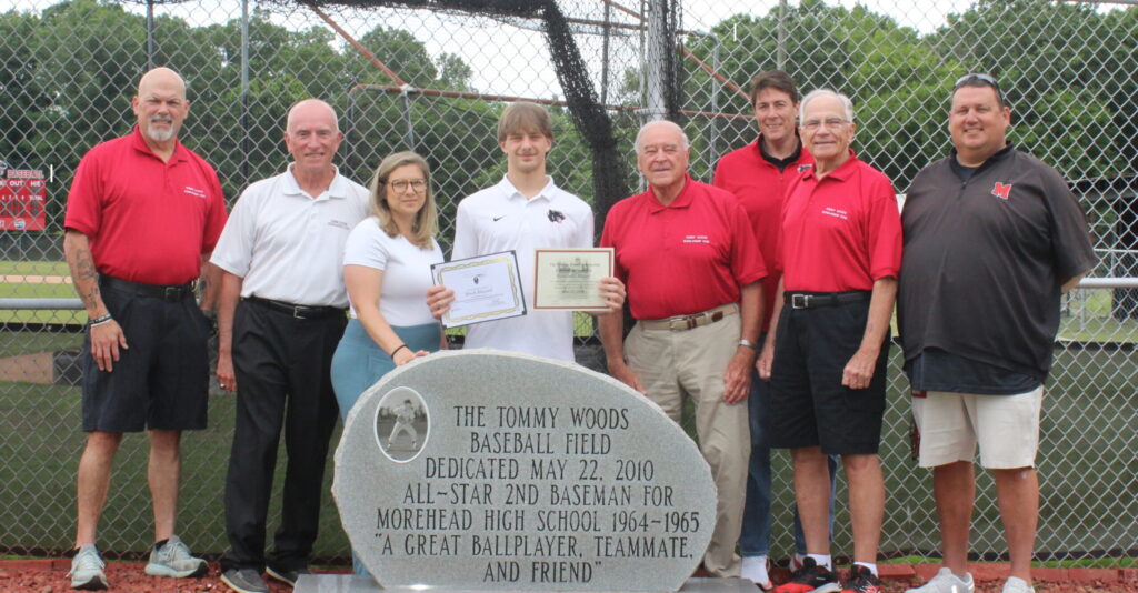 A group of people standing around a scholarship recipient who is holding two certificates